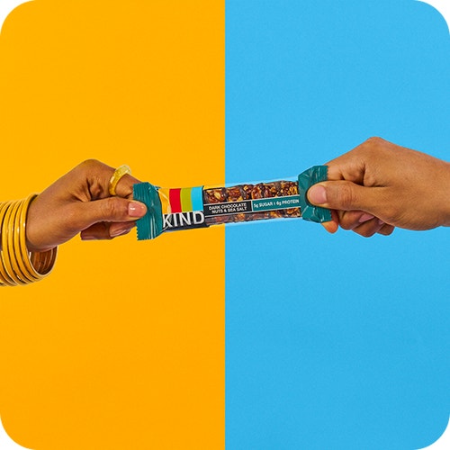 Two hands sharing a KIND snack bar